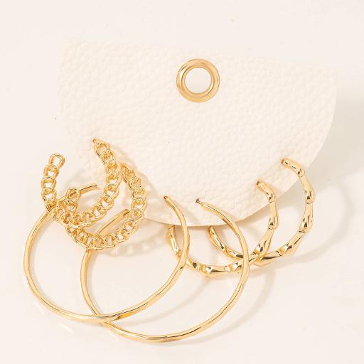 6 pairs of gold hoop earrings with pearls and cubic zirconia laying on a tan table cloth on a white earring package