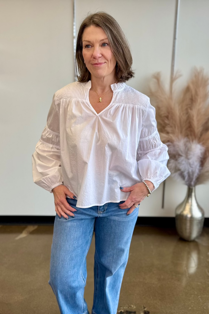 Close up photo of woman looking in the distance wearing a white flowy top and jeans.