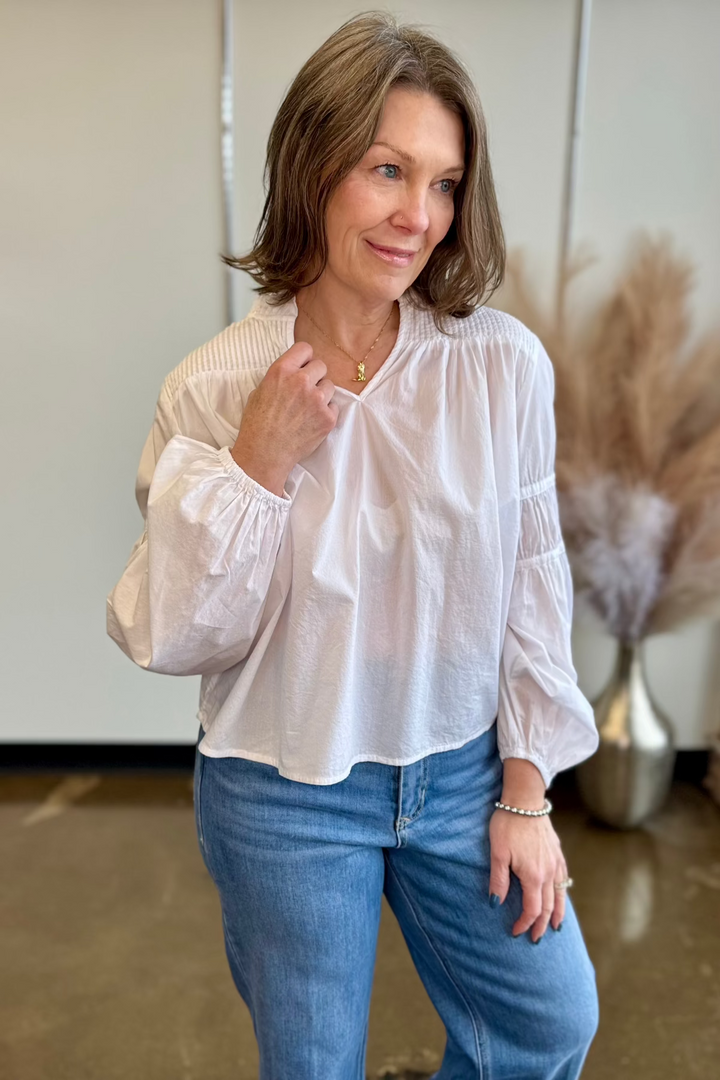 Close up of woman touching her white blouse at the neck  while looking in the distance.