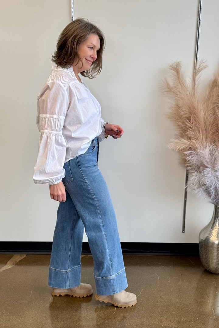 Side view of smiling woman wearing a white flowy top and blue jeans.