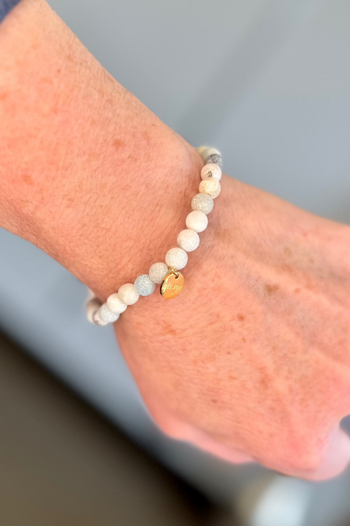 Close up of a woman wearing a light colored beaded bracelet with a small gold charm.