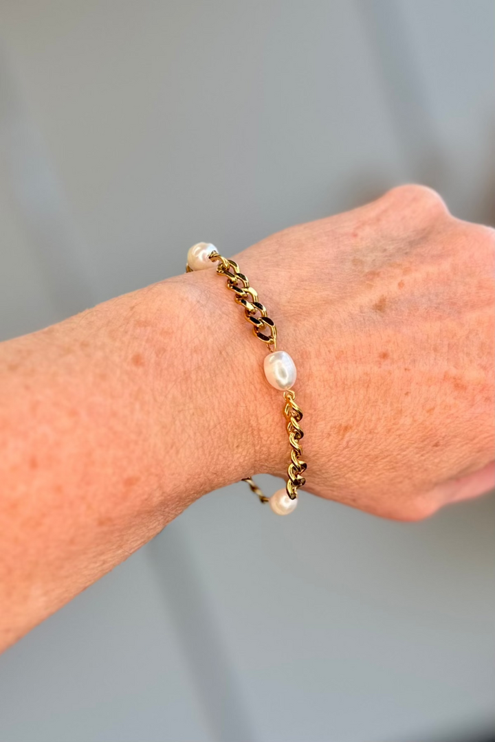 Close up of a woman wearing a gold chain bracelet with pearls.