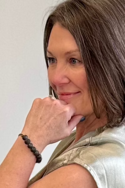 Woman looking off in the distance with her hand on her chin wearing a black beaded bracelet.