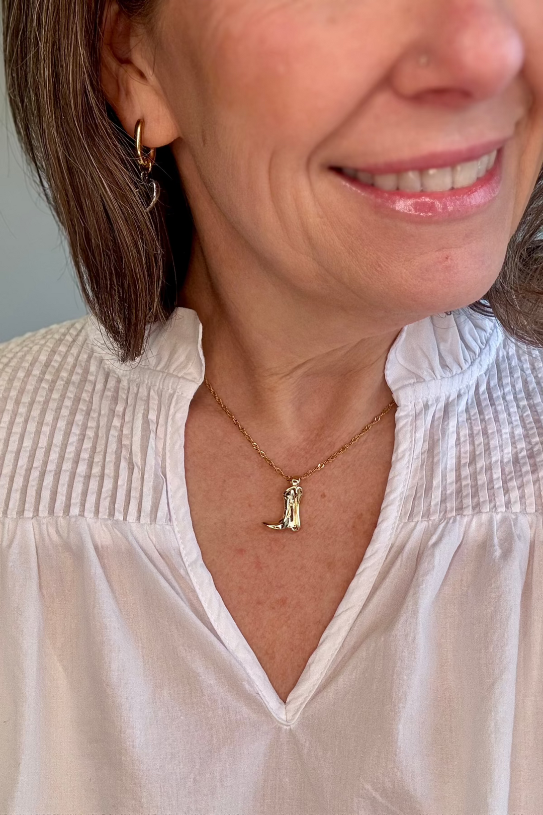 Woman wearing a gold cowboy boot necklace.