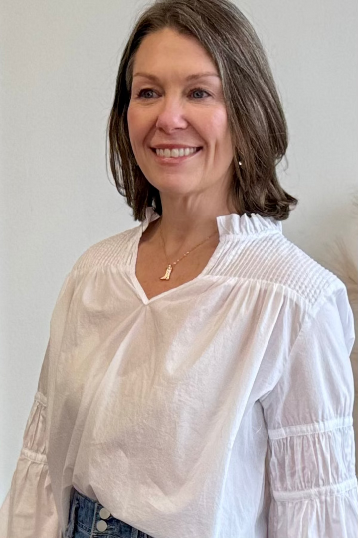 Woman wearing a white blouse and gold cowboy boot necklace.