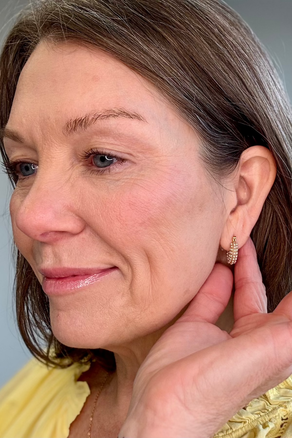 Close up of a woman modeling a gold and pearl earring holding her hand behind her ear.