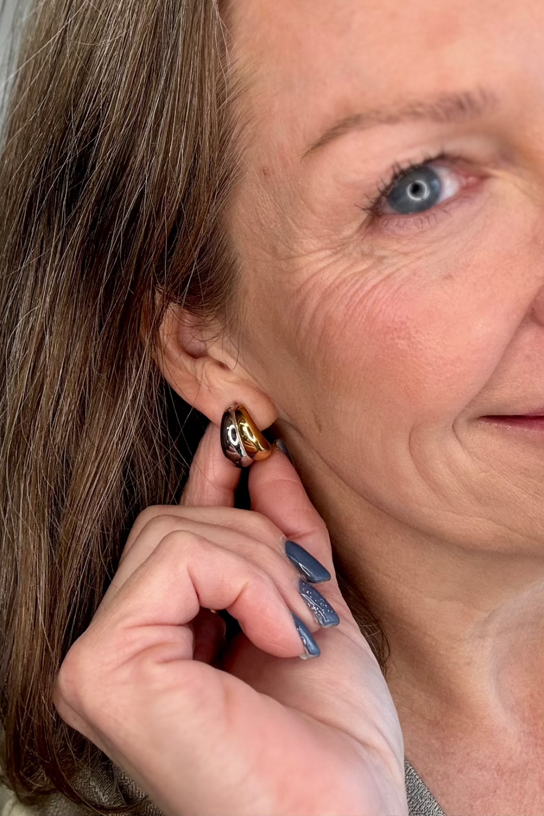 Half of a smiling woman's face showing a two tone earring.