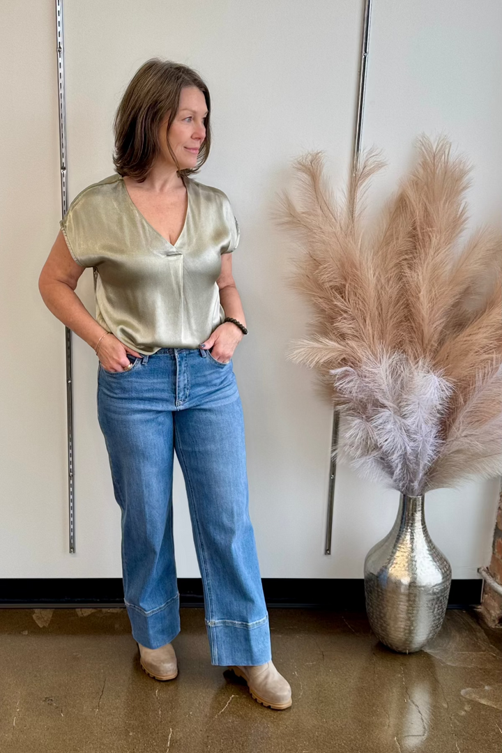 Woman standing with her hands in her pockets, in a full length photo, wearing a silky blouse and jeans and looking away from the camera.