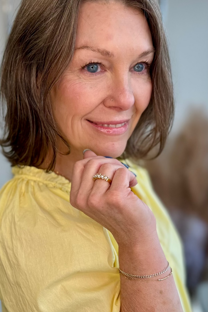 Smiling woman wearing a gold and pearl ring looking off in the distance.