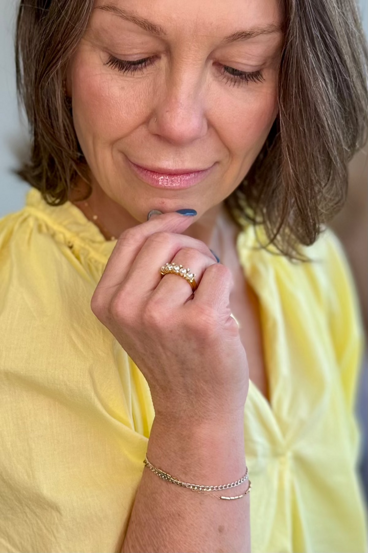 Woman looking down at a pearl and gold ring on her ring finger.