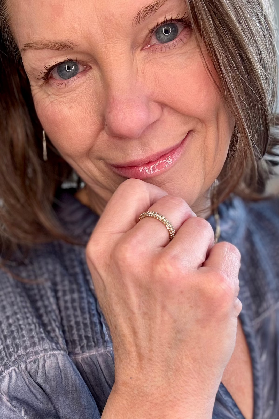 Close up of a woman with her hand on her chin showing a gold ring with crystals.