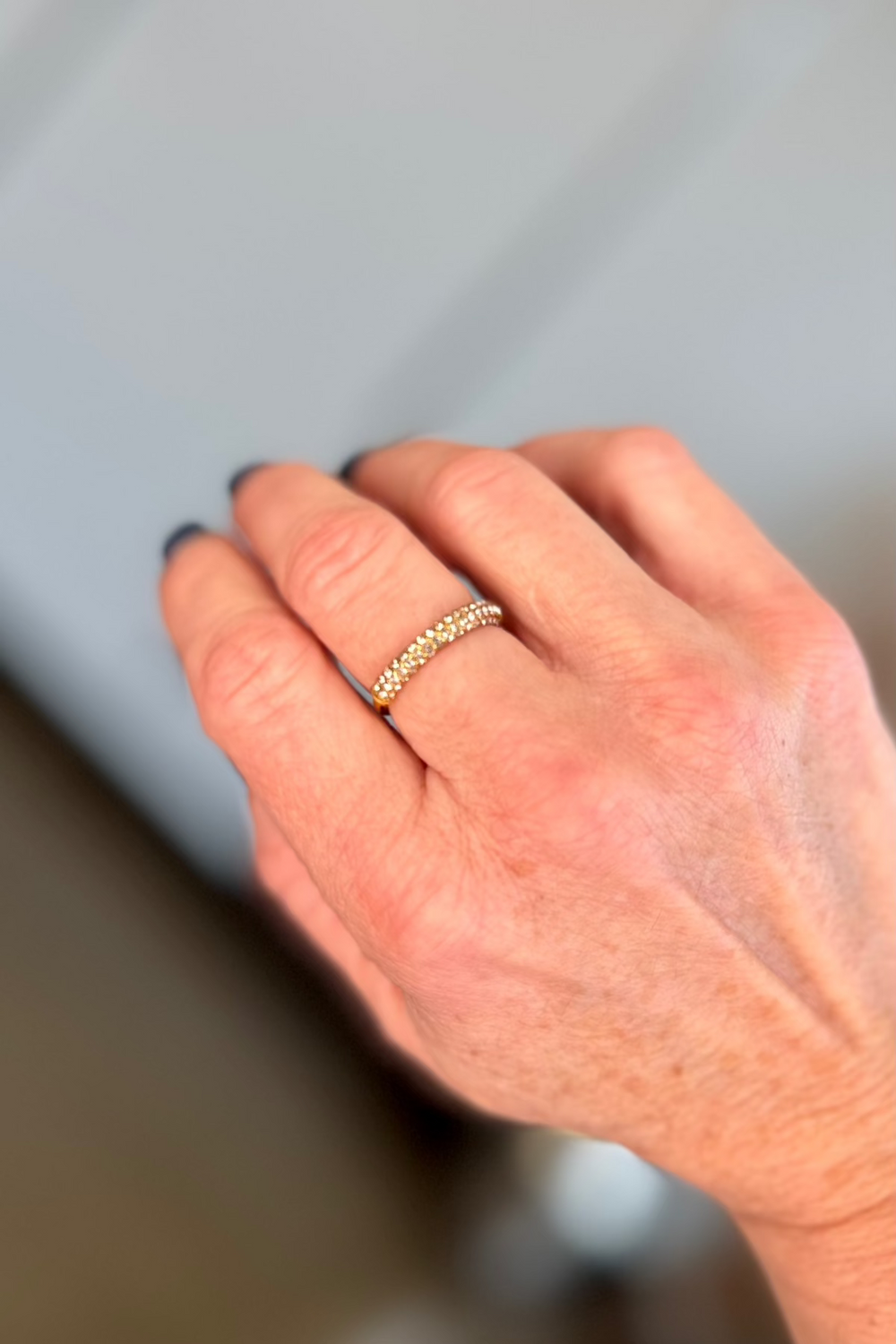 Close up of a woman's hand wearing a crystal and gold ring on her middle finger.