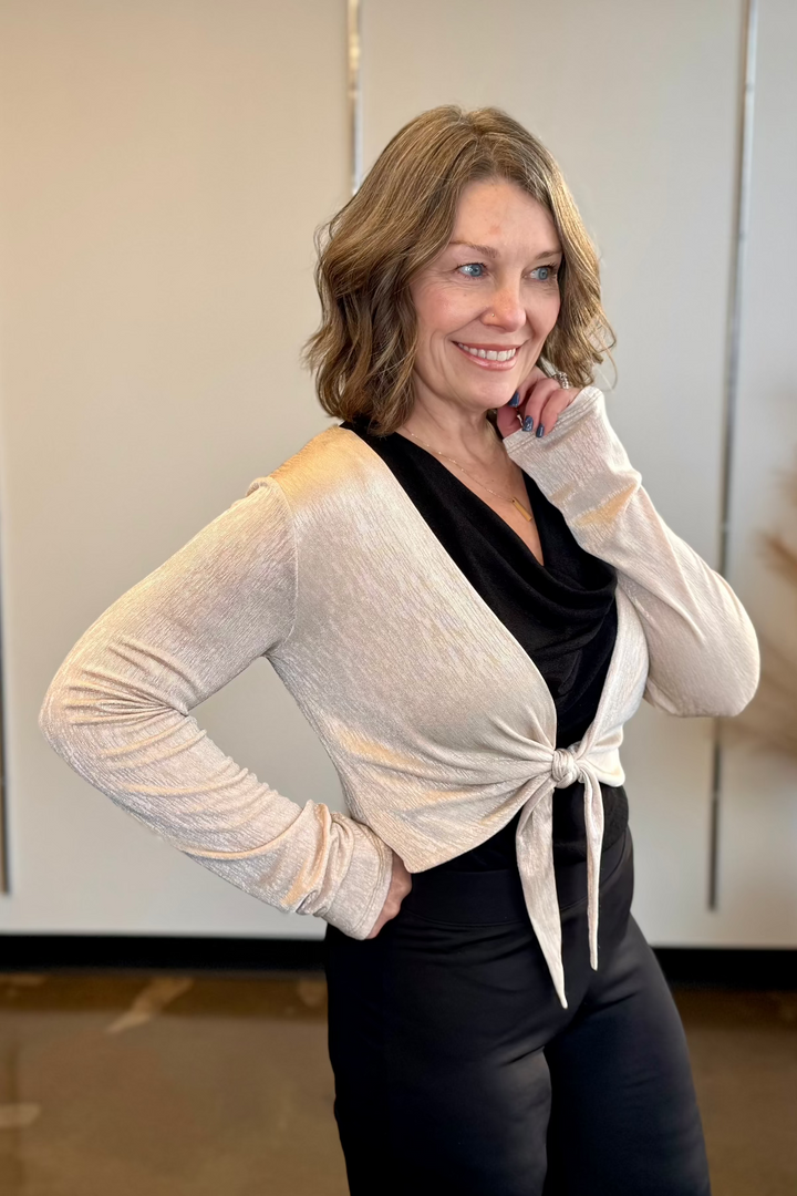 Close up of woman wearing a gold cropped cardigan and a black top and black pants.